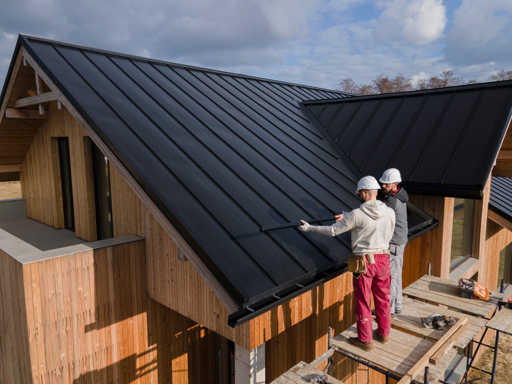 Craftsmen installing standing-seam metal roof on a new home